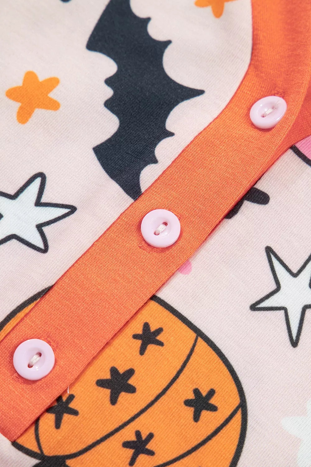 Close-up: orange button placket on dusty pink pumpkin-print long-sleeve pajama top