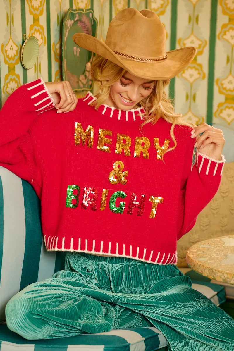 Red Christmas sweater with gold “MERRY & BRIGHT” sequin text and white fringe hem