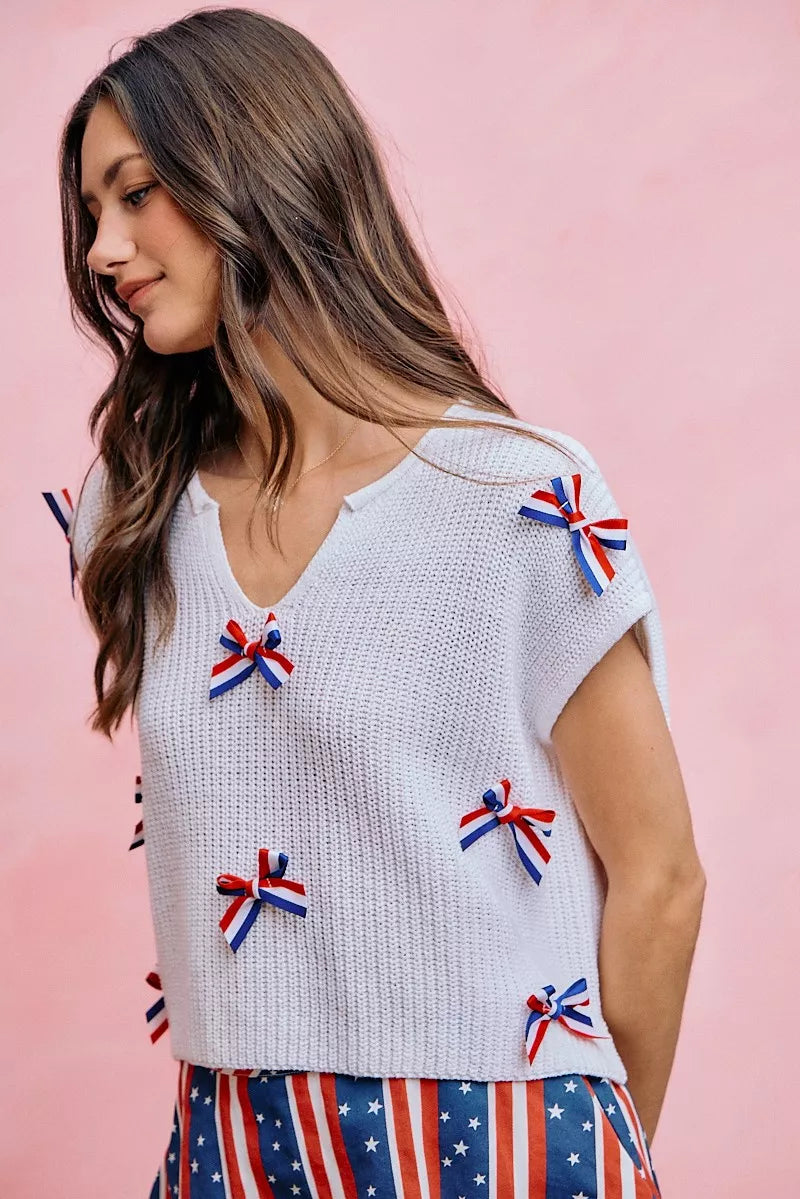 Off-white knit dolman sweater top with ribbon bow accents along the front and sleeve