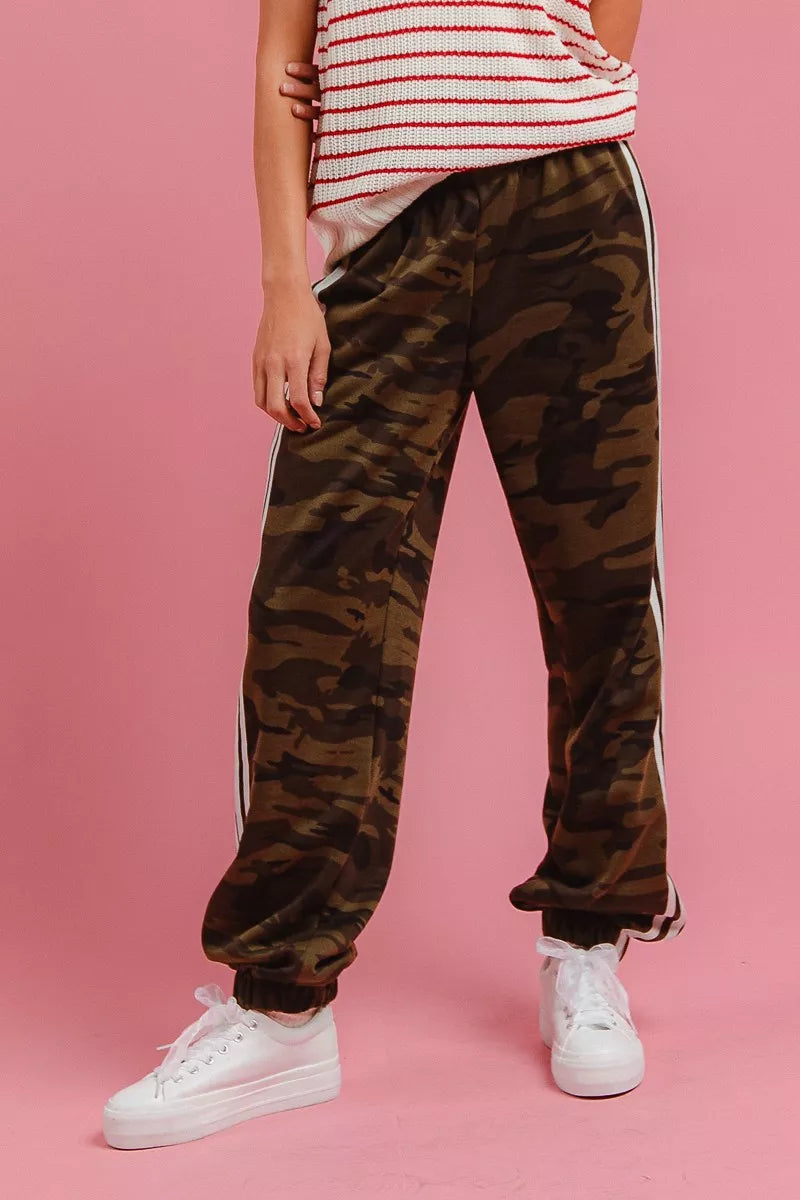 Camouflage track pants with white side stripes and elastic ankle cuffs.