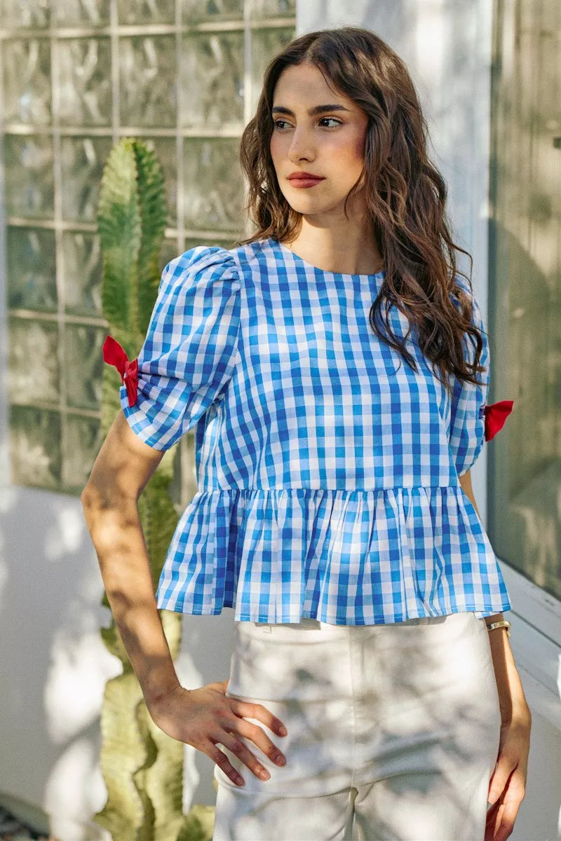 Blue gingham peplum blouse with short sleeves, gathered waist, and red bow ties on shoulders
