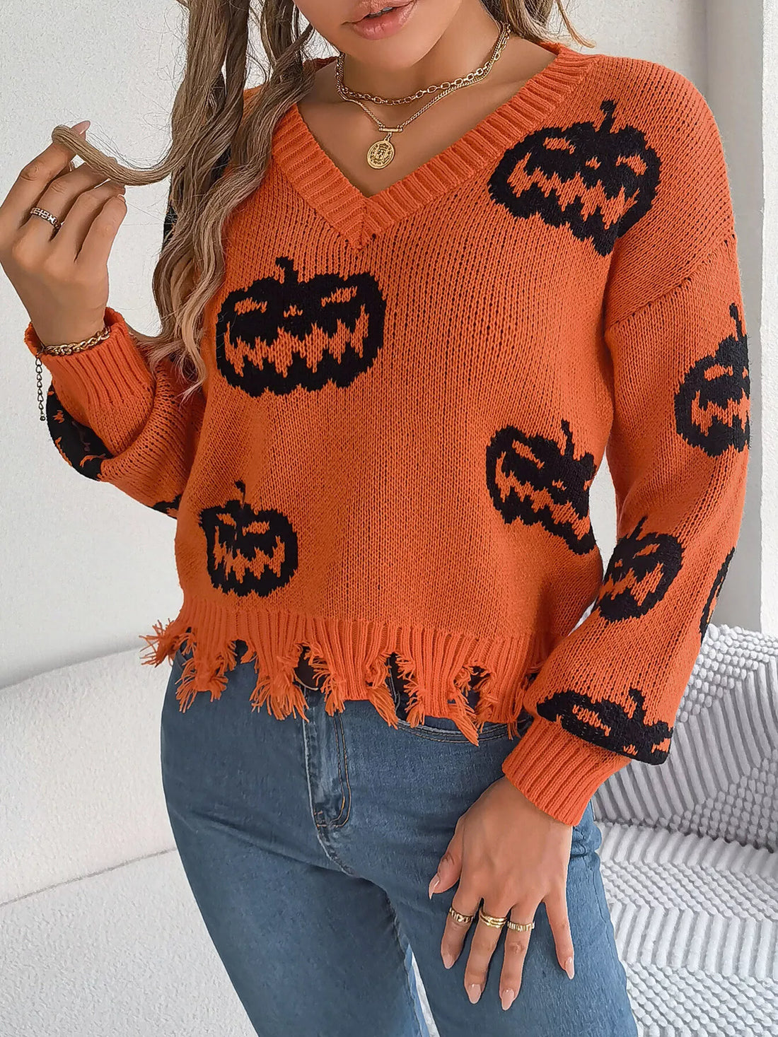 Orange V-neck pumpkin sweater with black jack-o’-lantern print and distressed frayed hem
