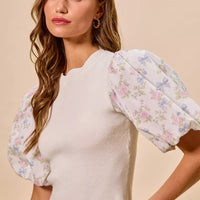 White knit top with puff floral sleeves and scalloped hem; crew neckline
