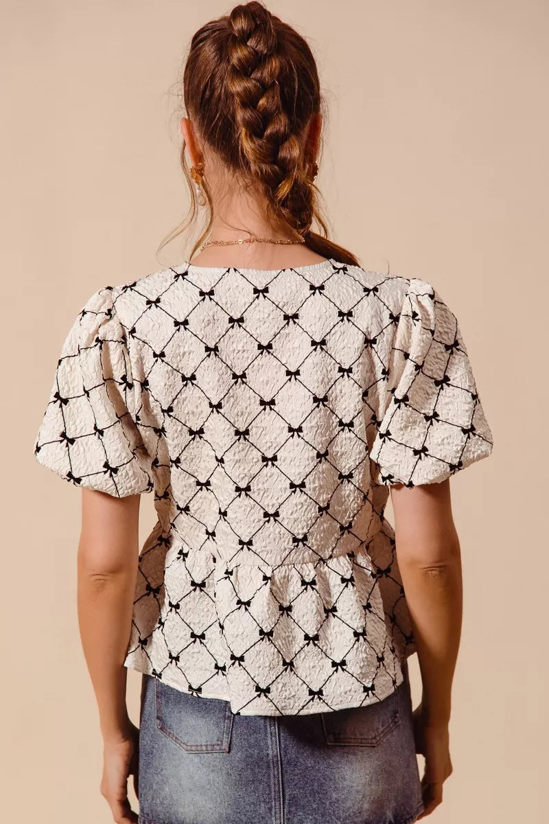 Back view of ivory woven peplum top with black ribbon bows and short puff sleeves.