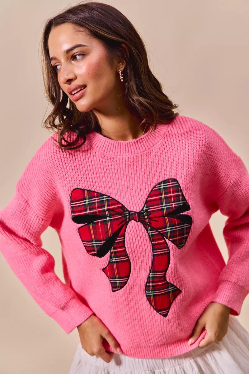 Pink knit Christmas sweater with oversized plaid bow graphic on front