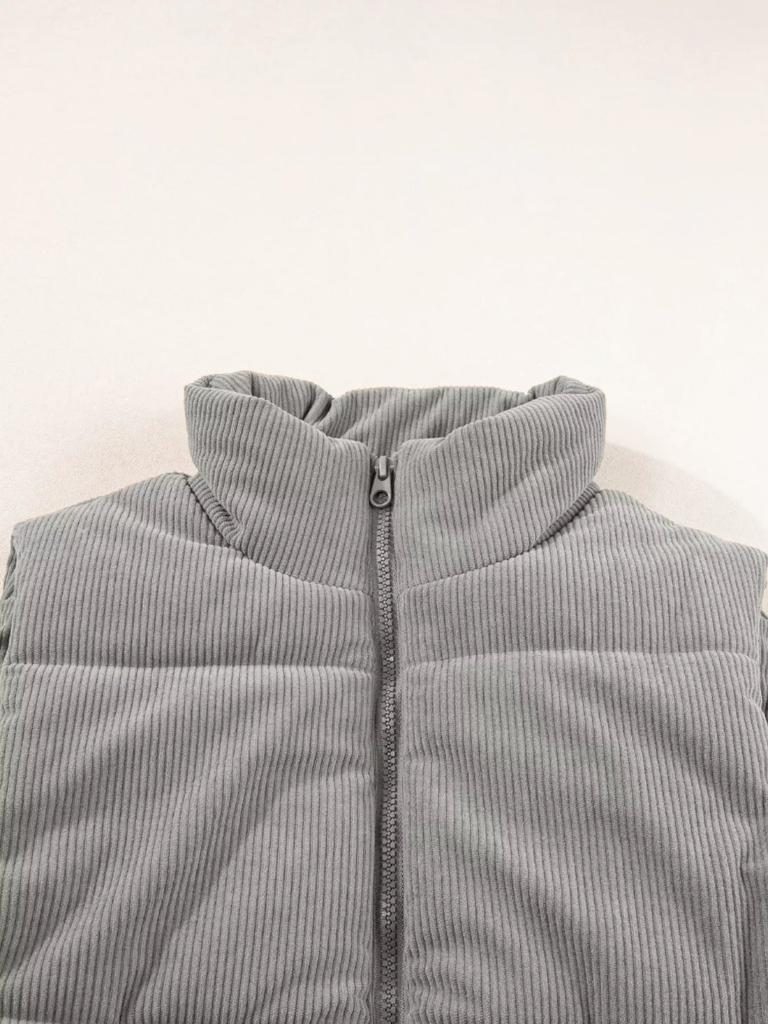 Gray corduroy stand-neck puffer vest close-up with front zipper and ribbed collar.