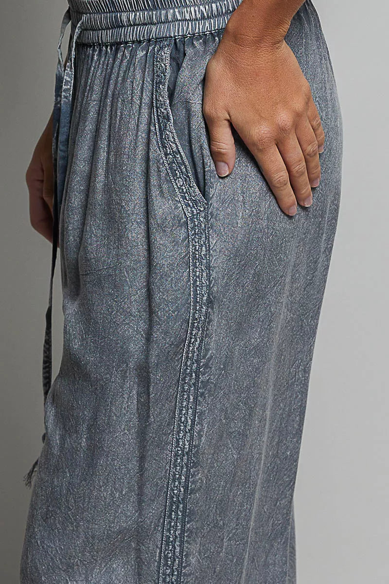Charcoal wide-leg woven pants close-up: embroidered panels and tassel drawstring