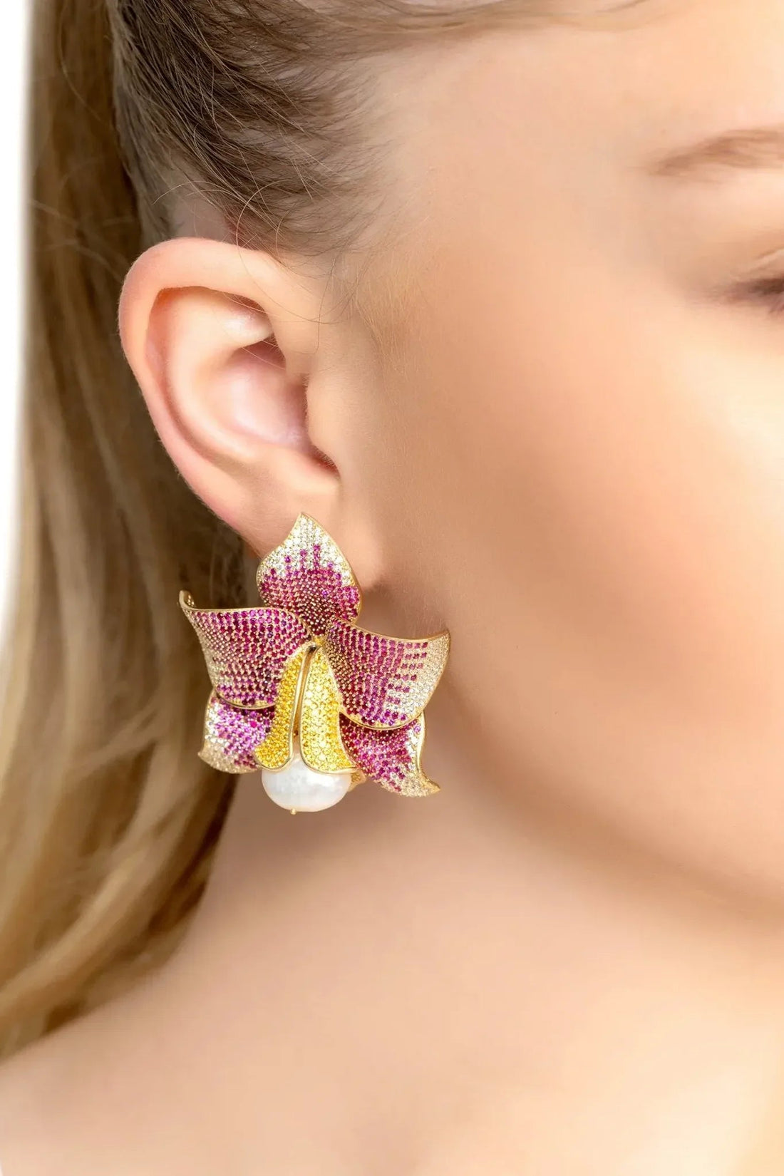 Gold-tone daffodil earrings with pink CZ floral top and faux pearl drop, shown on ear