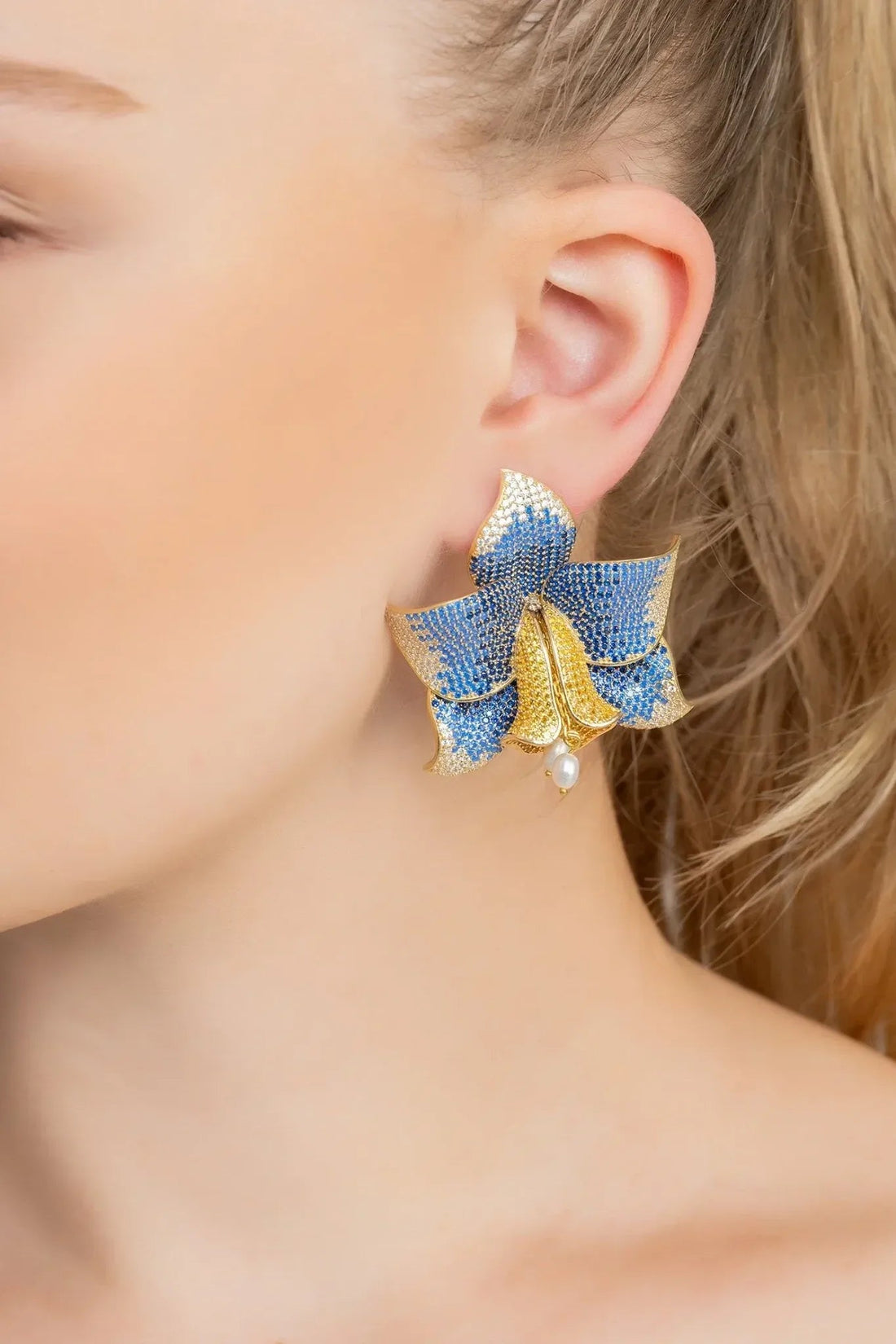Blue crystal daffodil earrings with gold-tone charm and pearl drop, close-up
