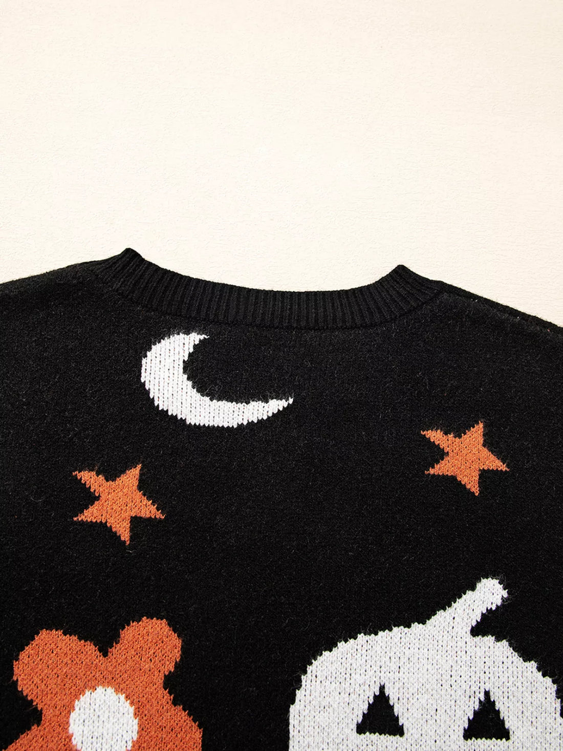 Black sweater close-up showing moon, orange star bursts, and pumpkin graphic on knit