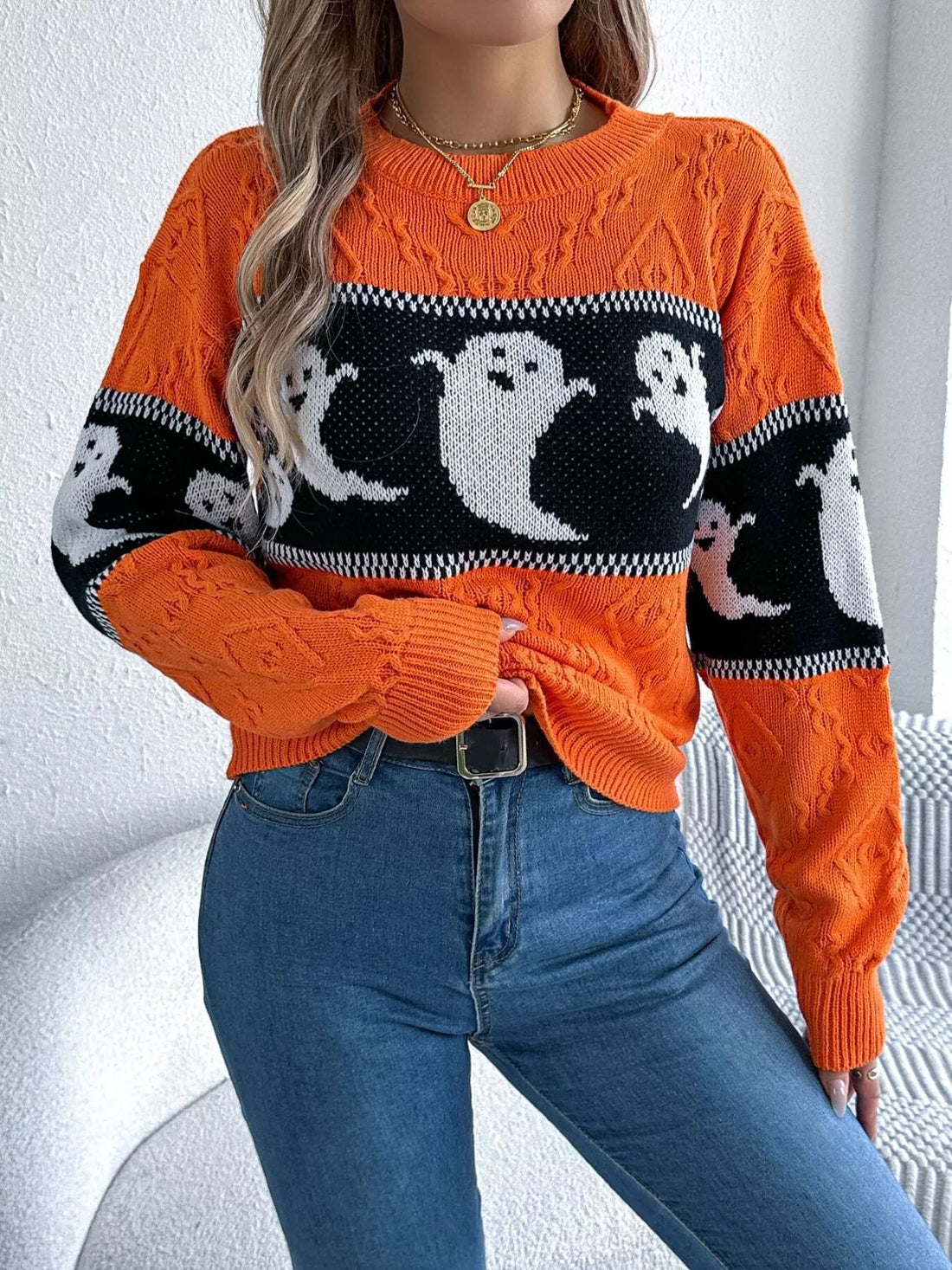 Orange ghost-pattern knit sweater with striped trim at the cuffs and neckline