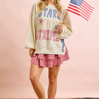 Cream sweatshirt with stars-and-stripes graphic, patch-style print, long sleeves; standing pose