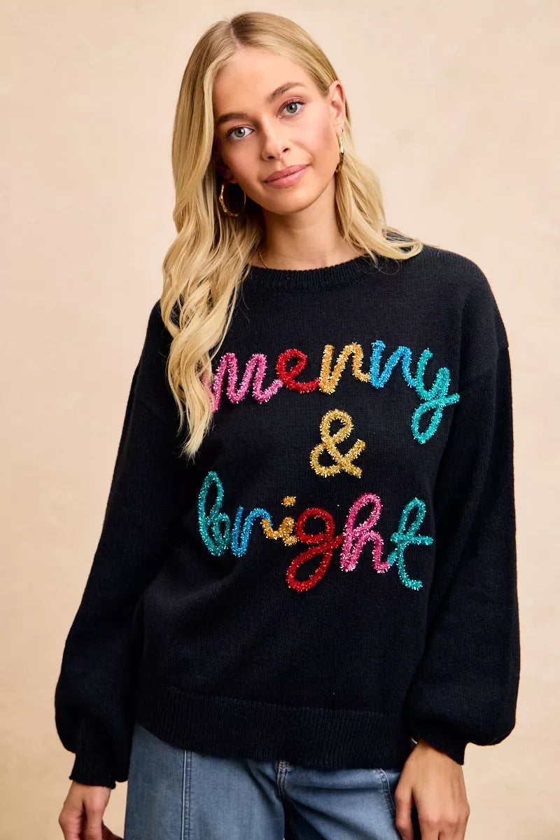 Black holiday sweater with multicolor tinsel "Merry & Bright" lettering at center front