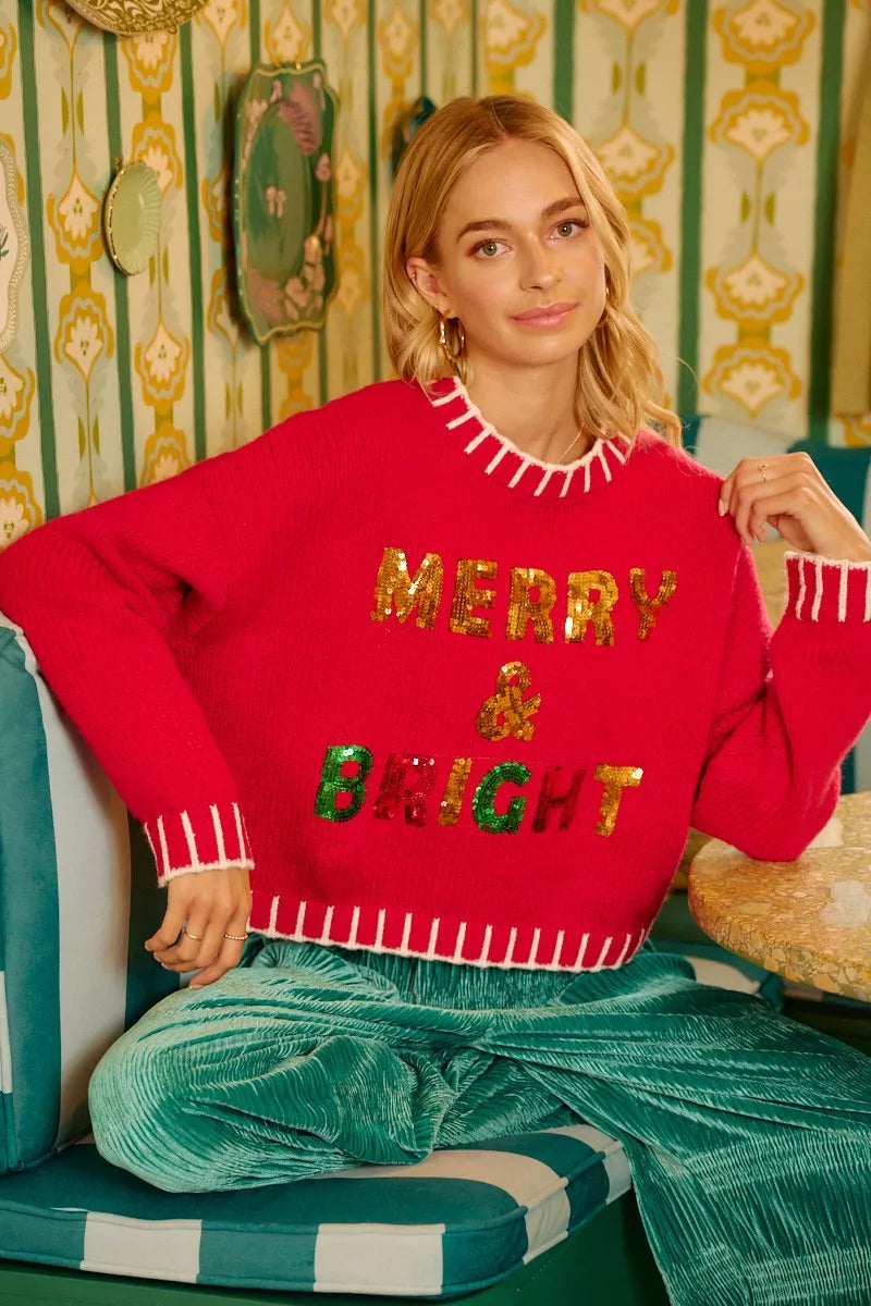Red holiday sweater featuring sequin "MERRY BRIGHT" text across the chest and hem trim.