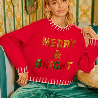 Red holiday sweater featuring sequin "MERRY BRIGHT" text across the chest and hem trim.