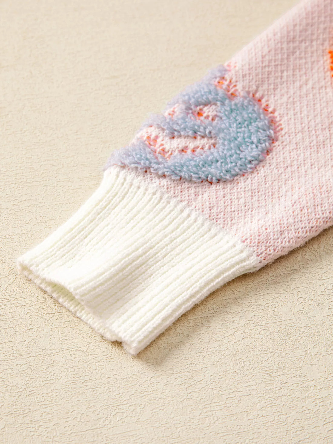 Dusty pink knit sweater cuff with ribbed white trim and blue ghost motif