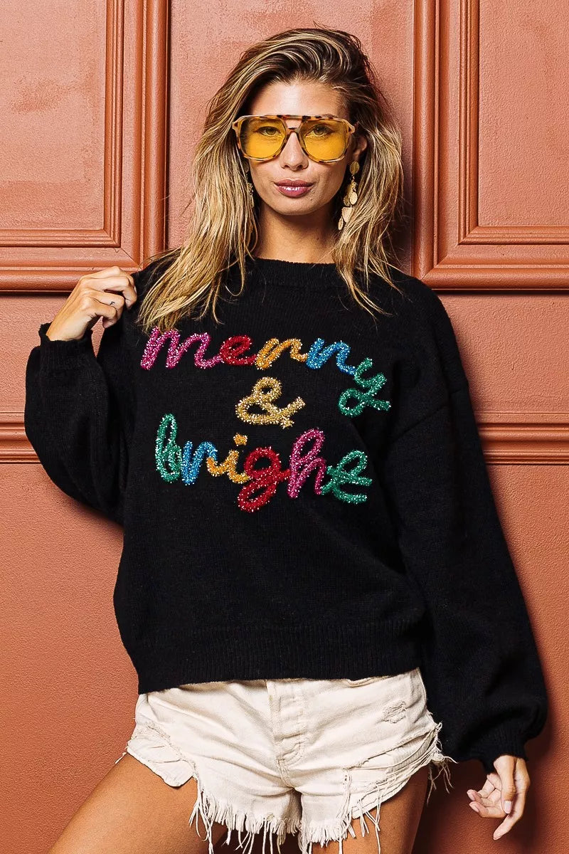 Black crewneck sweater with multicolor tinsel "Merry & bright" lettering, long sleeves.
