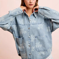 Light blue denim jacket close-up with white floral print, button front and chest pockets