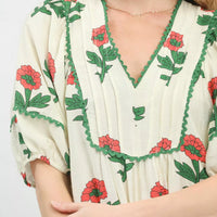 Cream floral midi dress close-up with scalloped V-neck and green trim, red blossoms
