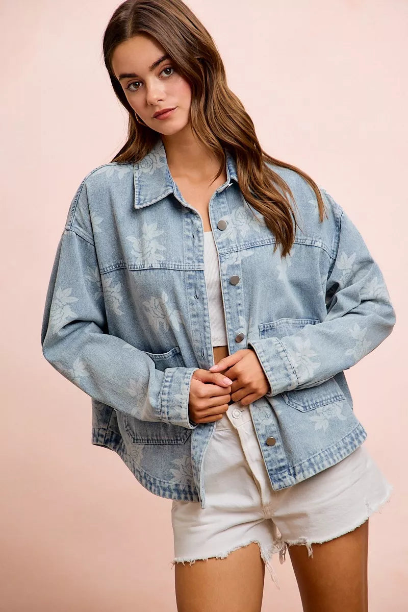 Light blue washed denim jacket with white floral print, button front, and flap chest pockets