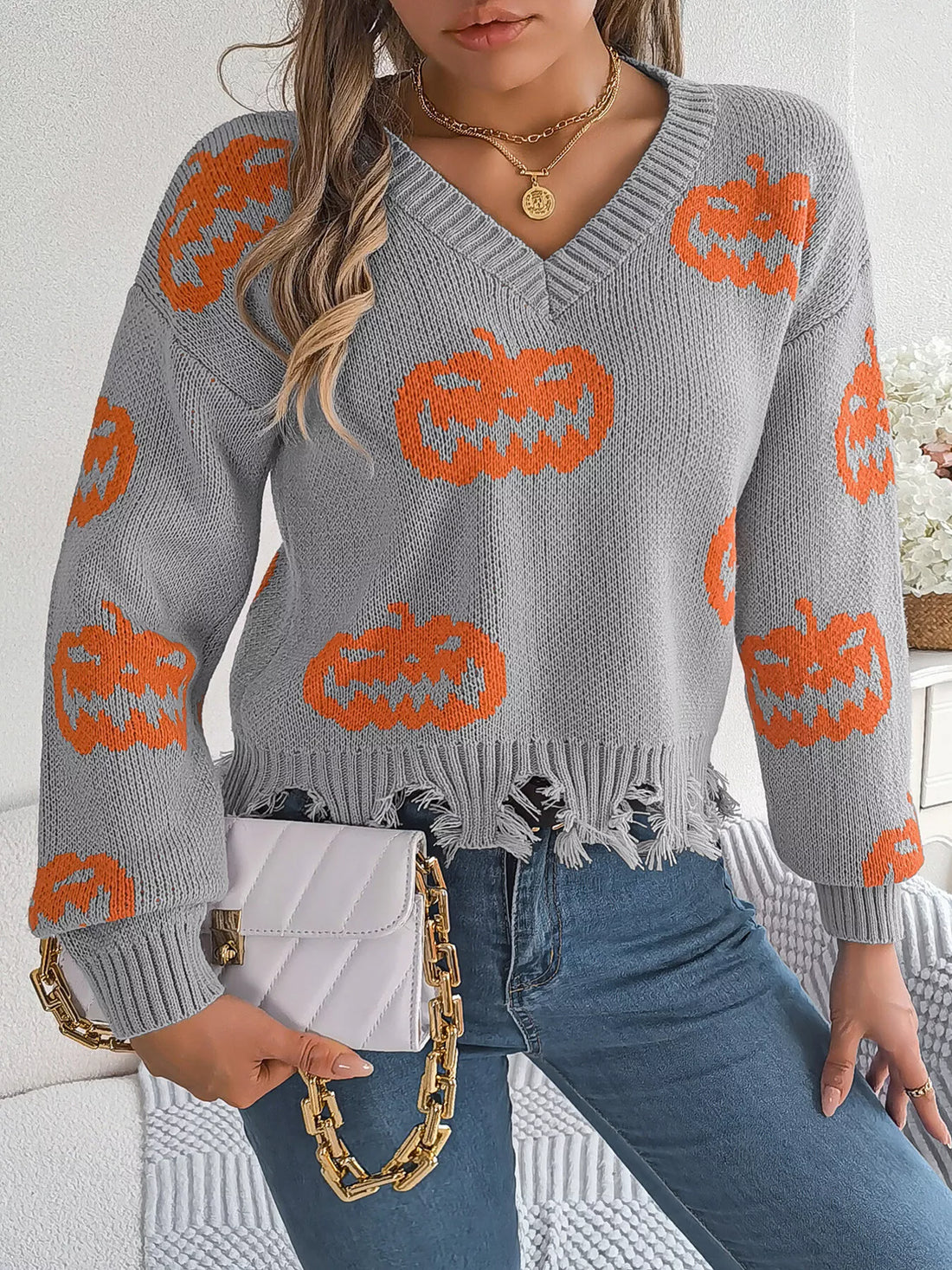 Gray knit V-neck sweater with orange pumpkin pattern and distressed fringe hem