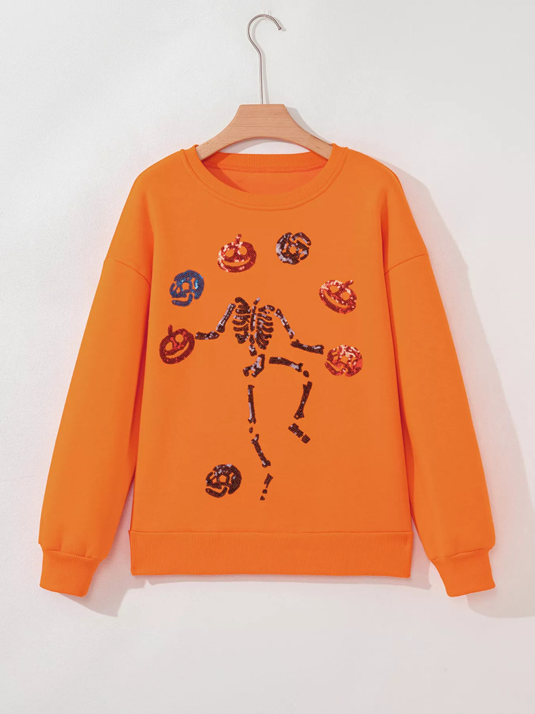 Orange Halloween crewneck sweatshirt with sequin skeleton and critter icons, on hanger