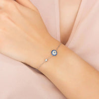 Silver chain evil eye bracelet on wrist with blue round charm