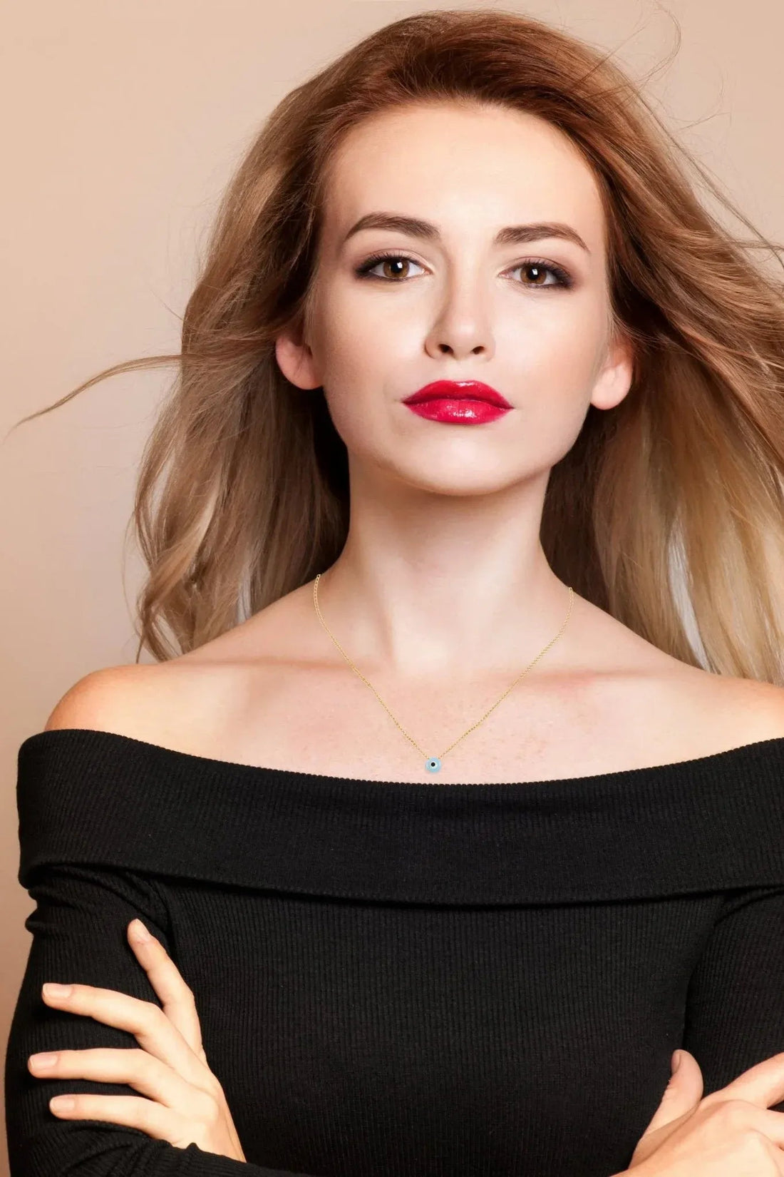 Gold evil-eye pendant necklace on model with off-shoulder black top, blue opalite charm