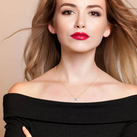 Gold evil-eye pendant necklace on model with off-shoulder black top, blue opalite charm