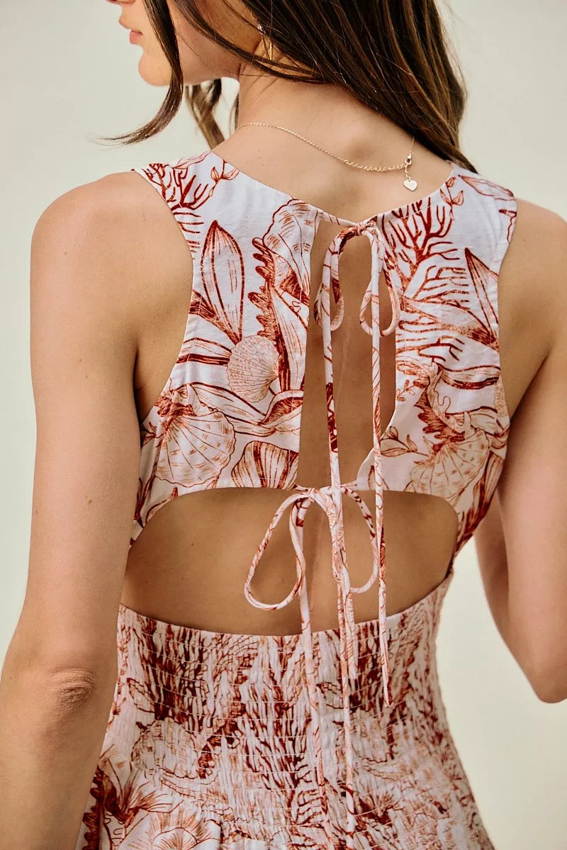 Back view of coral and white shell-print mini dress with smocked waist and tied open-back
