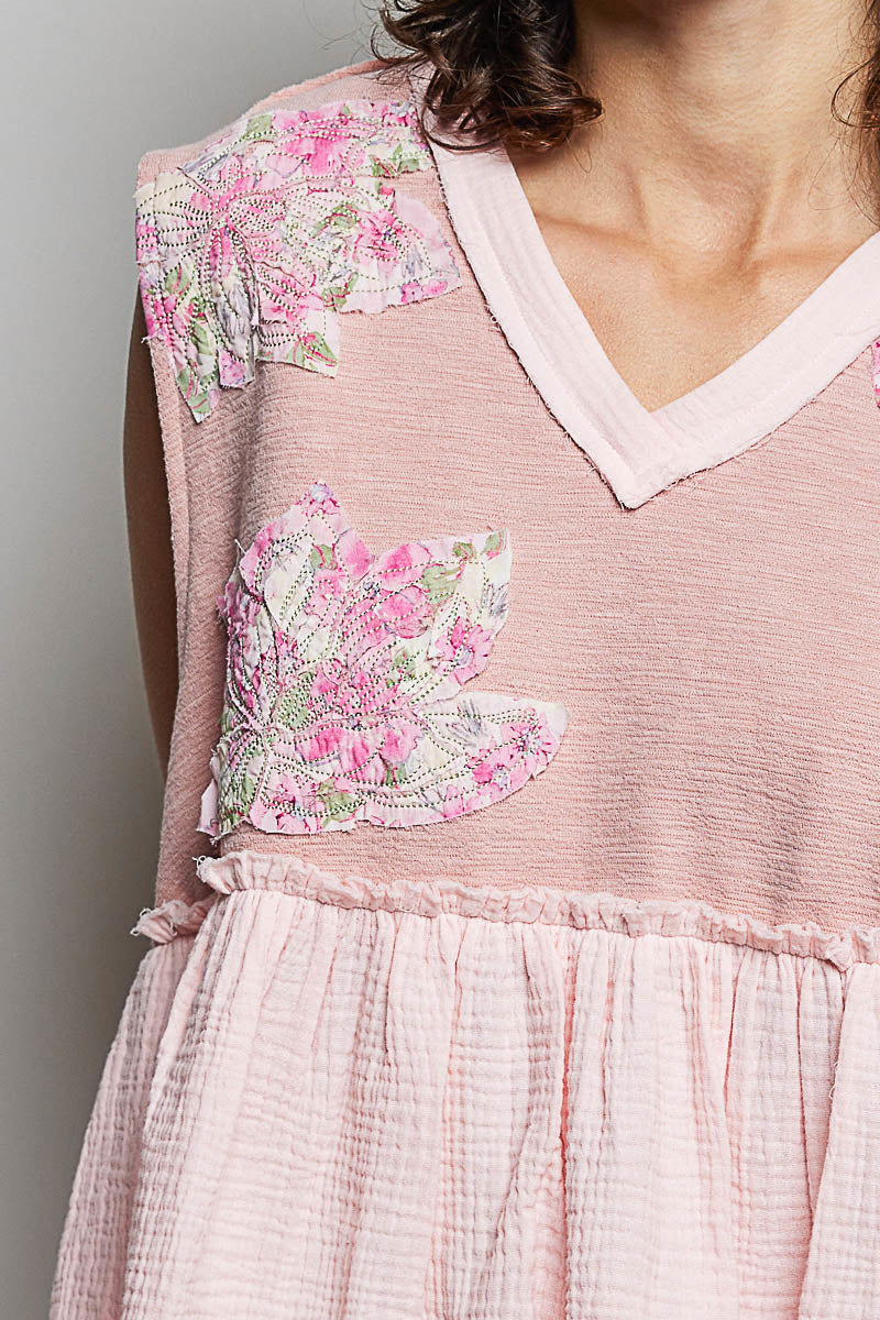 Powder pink sleeveless top close-up with V-neck trim, floral patch and raw-edge ruffle