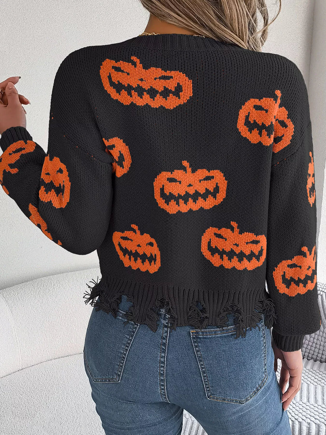 Black V-neck sweater with orange pumpkin pattern, distressed frayed hem on back view