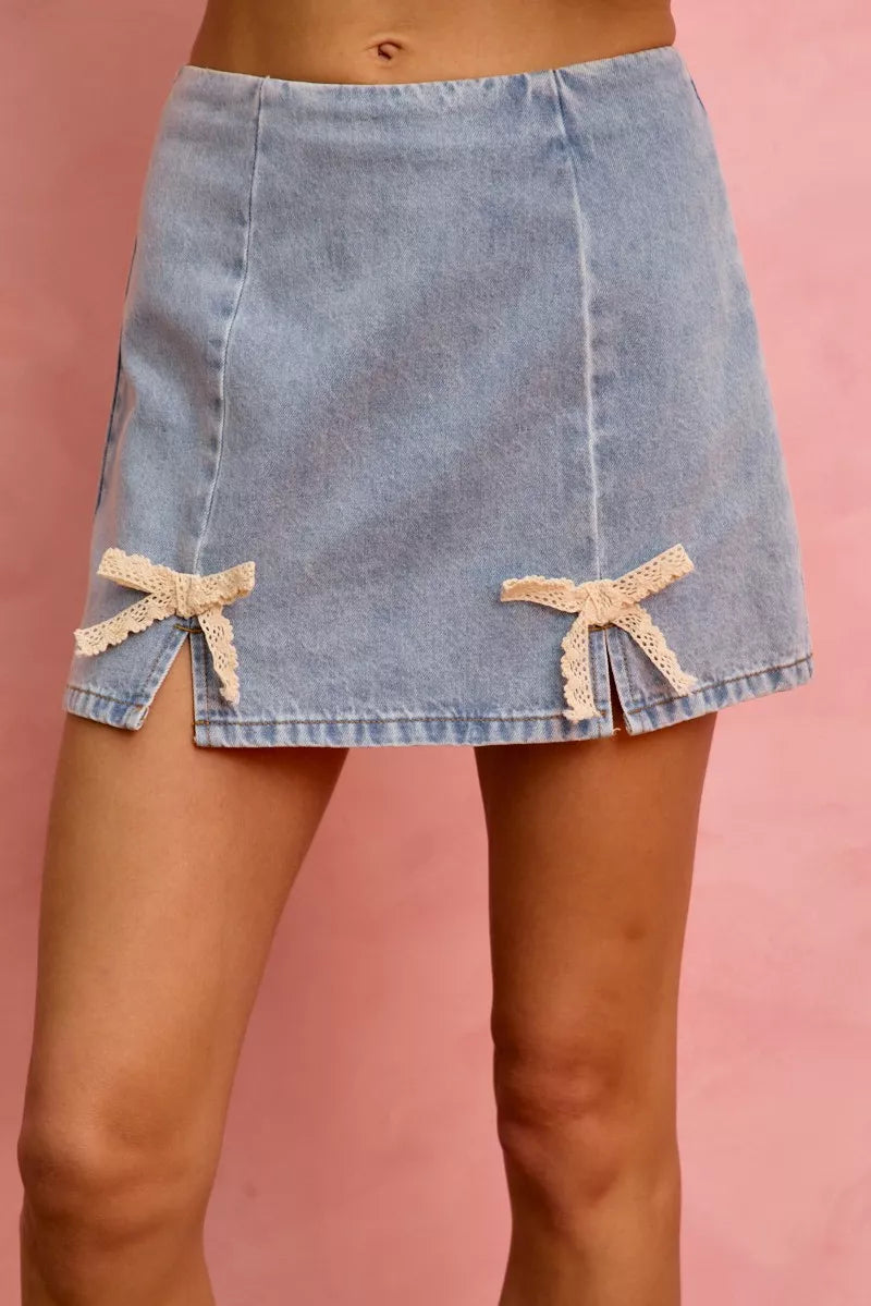Light blue denim mini skirt with two lace ribbon bows on the front hem.