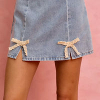Light blue denim mini skirt with two lace ribbon bows on the front hem.