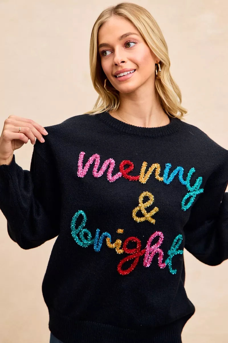 Black sweater featuring multicolor tinsel "Merry & Bright" text across the front