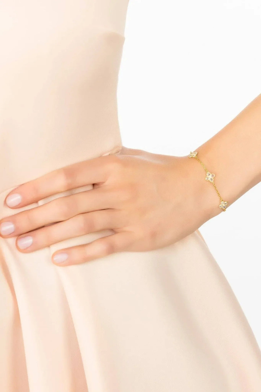 Gold clover charm bracelet on wrist with three white crystal flower details