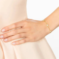 Gold clover charm bracelet on wrist with three white crystal flower details
