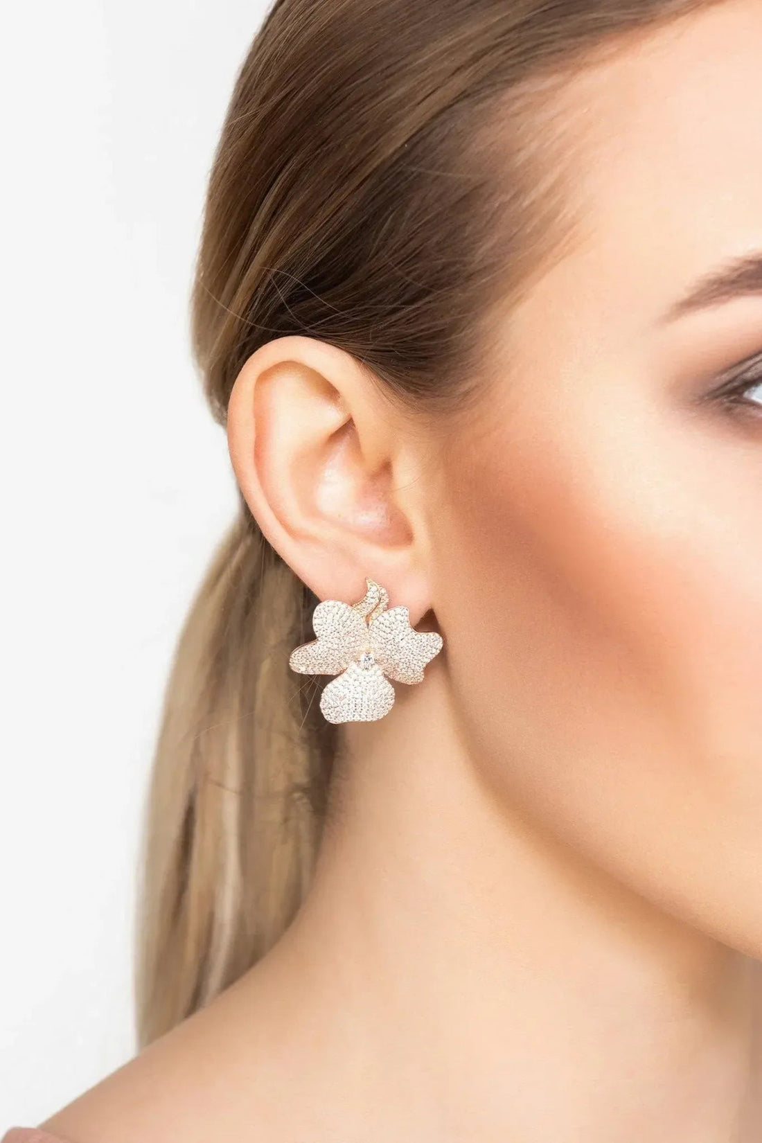 Large four-petal flower stud earrings in rose-gold tone on a model’s ear
