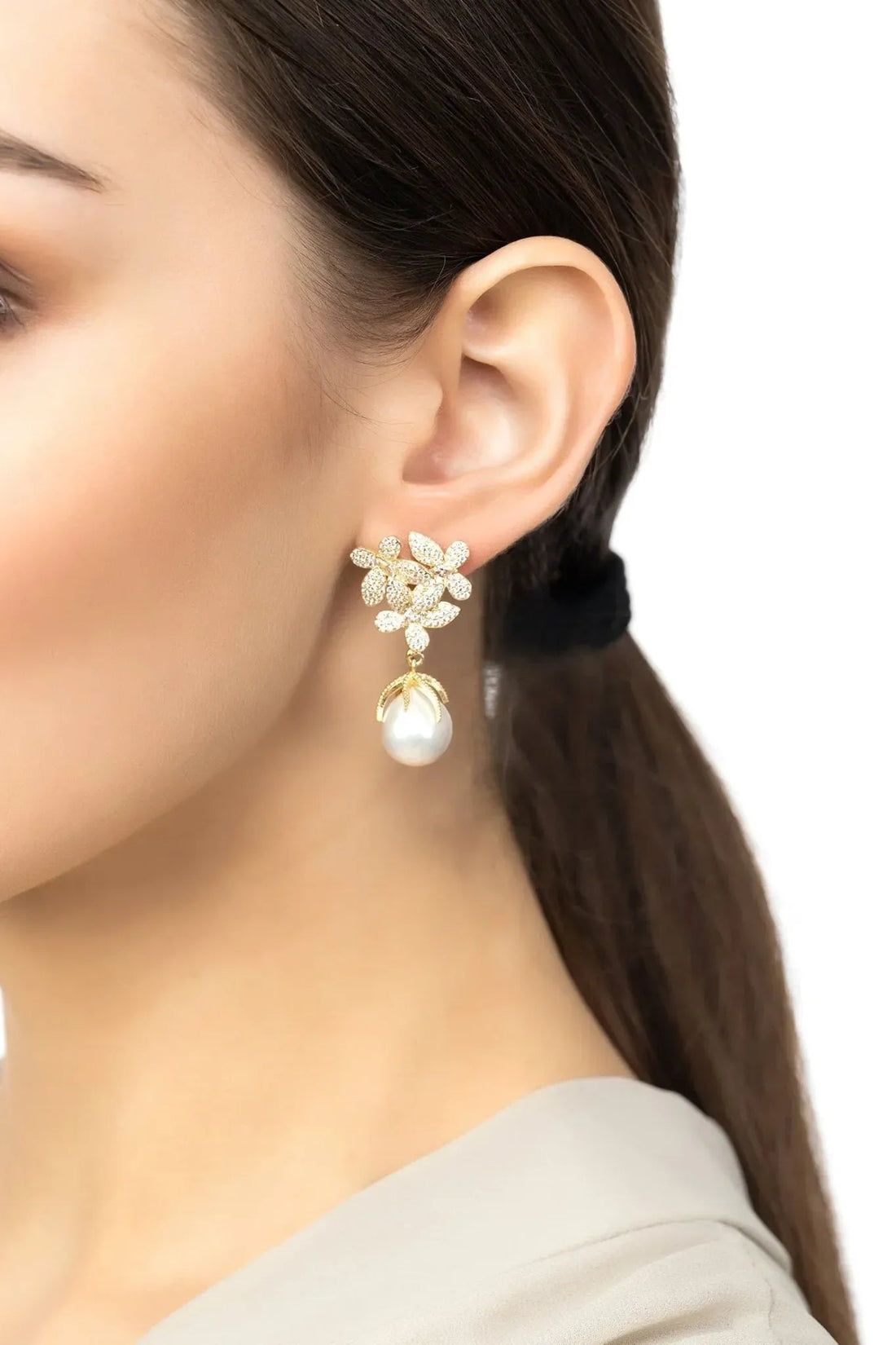 Gold floral earrings with white pearl drop, worn on model’s ear