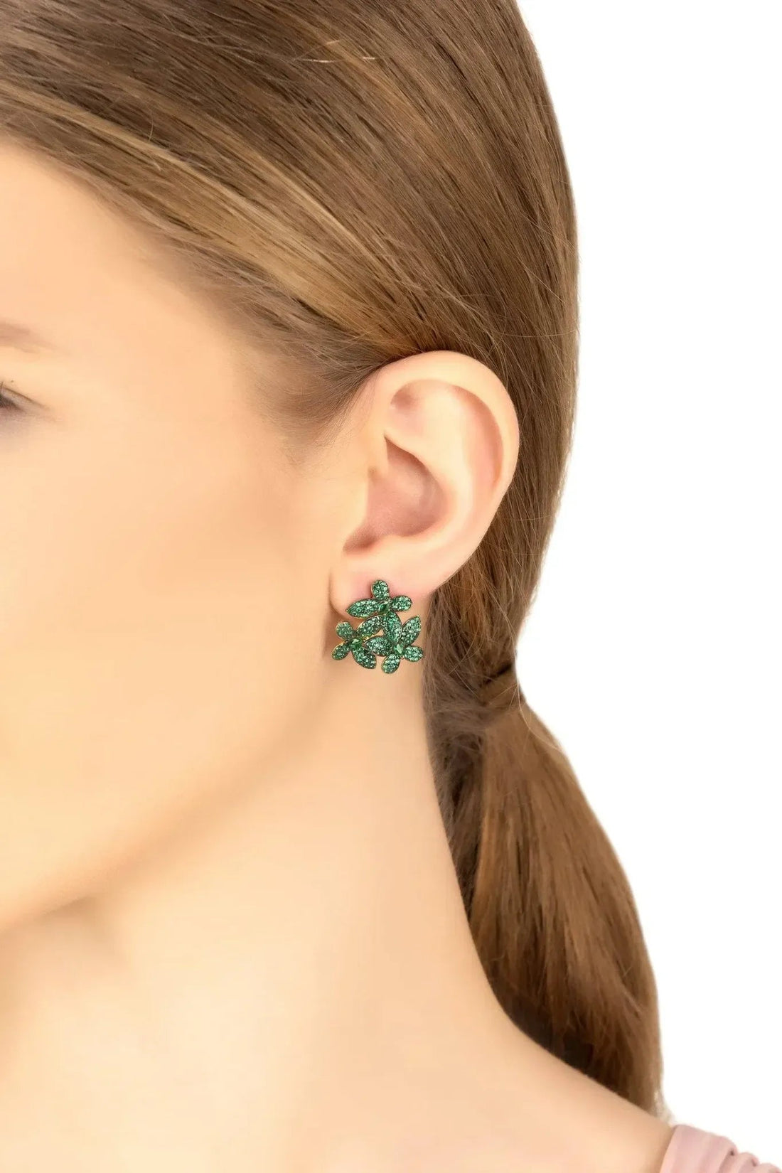 Emerald-green flower stud earrings with gold-tone posts on an ear