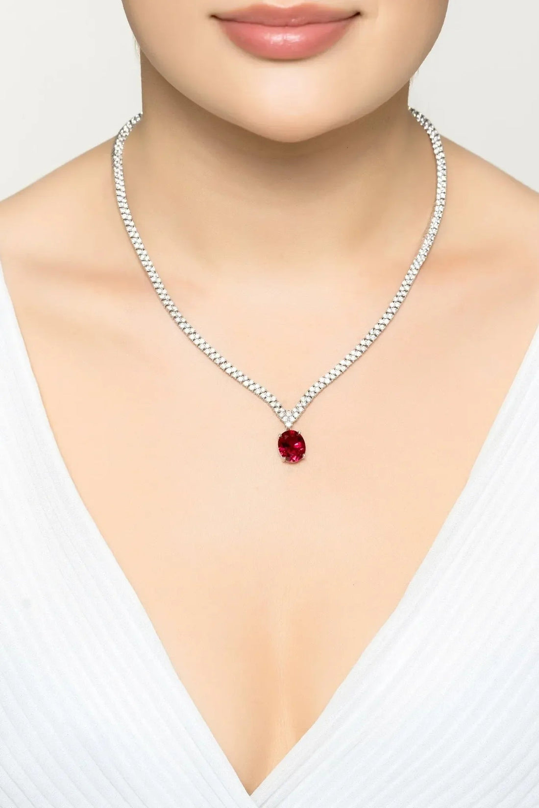 Silver tennis necklace with ruby oval pendant centered on a rhinestone chain