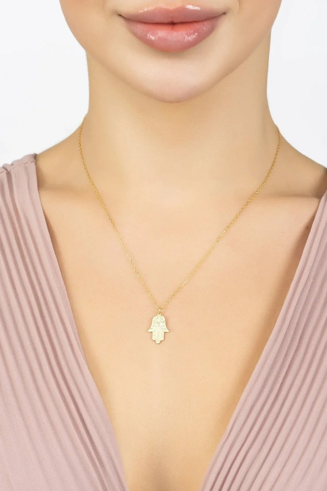 Gold-tone hamsa pendant necklace with small hand-shaped charm worn at neckline