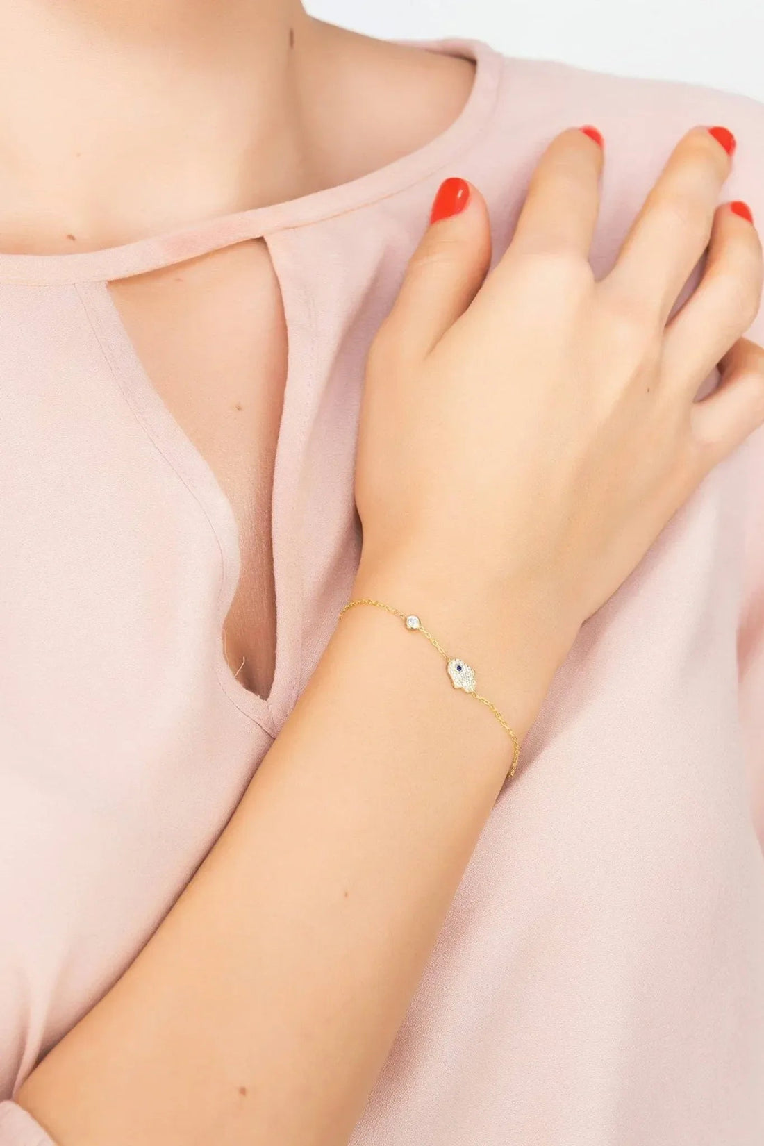 Rose gold hamsa hand bracelet with small blue stone charm on wrist
