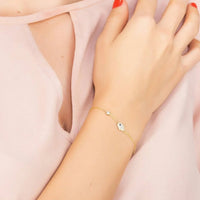 Rose gold hamsa hand bracelet with small blue stone charm on wrist