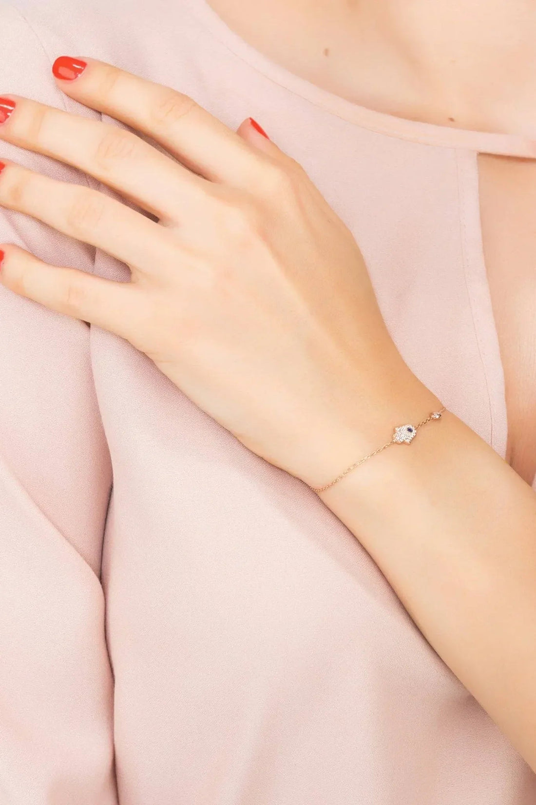 Rose gold hamsa hand bracelet with small blue stone charm, worn on wrist