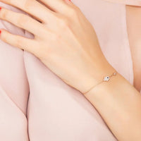 Rose gold hamsa hand bracelet with small blue stone charm, worn on wrist