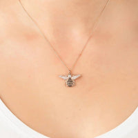 Gold-tone bee pendant necklace with crystal accents, shown on a neckline