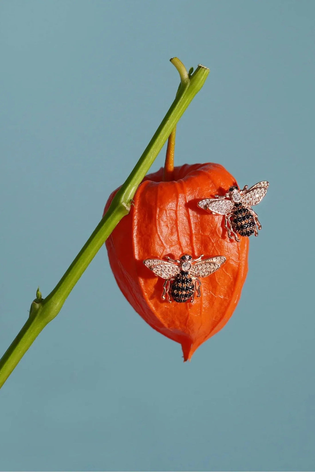 Rose-gold bee stud earrings with crystal wings on a decorative pepper