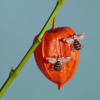 Rose-gold bee stud earrings with crystal wings on a decorative pepper
