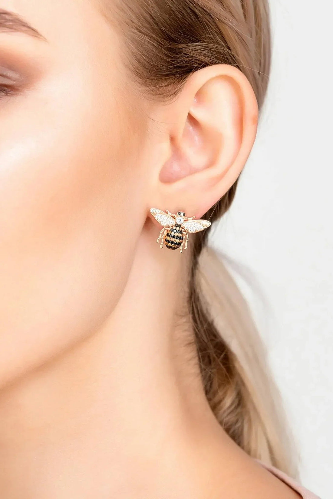 Rose-gold bee stud earrings on ear, crystal bee and wing details